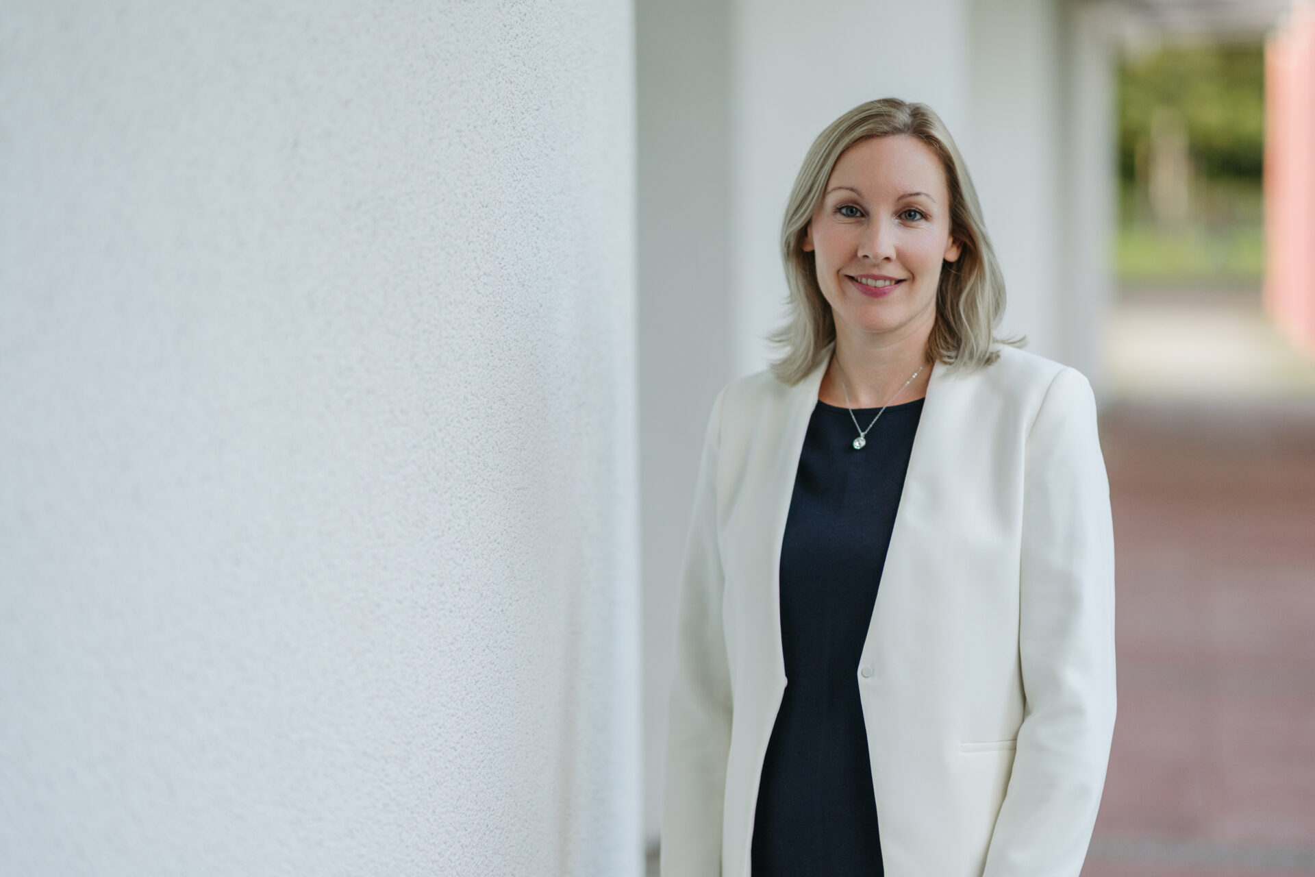 Karin Leitner, neue Linzer Sozial- und Sportstadträtin, posiert lächelnd in einem eleganten weißen Blazer und dunklem Oberteil vor einer hellen Wand.